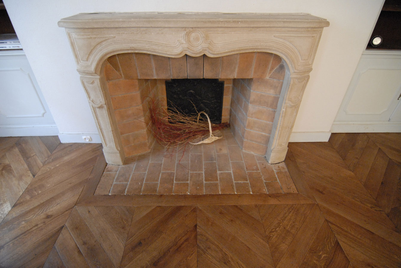 Parquet Chevron chÃªne en finition patinÃ©e vieillie. On voit nettement que les lames de parquet passent sous les plinthes restÃ©es en place.